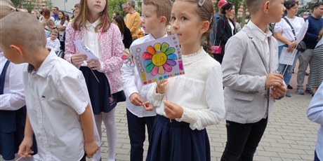 Powiększ grafikę: Grupa uczniów ubranych elegancko. Jedna uczennica trzyma papierowy kwiat z napisem 1a.