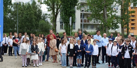 Powiększ grafikę: Uczniowie, nauczyciele i rodzice stoją przed budynkiem szkoły.